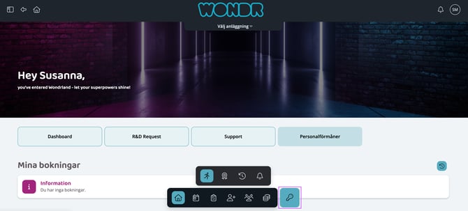 En startsida för webbportalen "WONDR" med välkomsttexten ”Hey Susanna”. Sidan har en mörk bakgrundsbild som föreställer en upplyst korridor eller träningslokal. Under välkomsthälsningen finns fyra stora knappar: ”Dashboard”, ”R&D Request”, ”Support” och ”Personalförmåner”. Under sektionen ”Mina bokningar” visas ett meddelande om att det inte finns några bokningar. Längst ner i bild syns två svarta flytande menyfält med olika ikoner för navigering. En separat blå ikon som föreställer en nyckel är inramad med en lila rektangel till höger om menyerna.